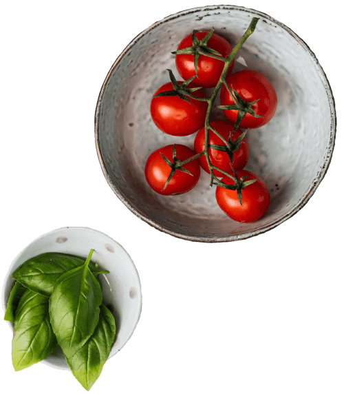 A bowl of tomatoes and a plate with basil.